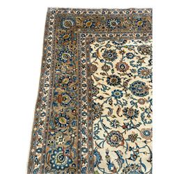 Persian Kashan rug, pale gold ground, the field decorated in blue with trailing branches and stylised plant motifs, the main border band with matched repeating design