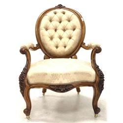 Late Victorian mahogany open armchair, floral carved crest rail over oval buttoned back, scrolled and leaf carved arm terminals, shaped apron and cabriole supports terminating in ceramic castors, upholstered in ivory floral damask, W64cm