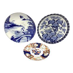 Late 19th/early 20th century Japanese charger decorated in blue and white with chrysanthemum within a scalloped border D47cm, another with a river landscape, buildings etc D46cm, and an Imari plate D33cm (3)
