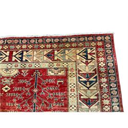 Afghan Kazak crimson ground rug, the field decorated with stylised geometric tree and animal motifs and octagonal and rectangular shapes enclosing stars, the multi-band ivory border with repeating shapes and stylised flower heads