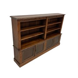 Late 19th to early 20th century oak standing bookcase, the projecting cornice with lunette and foliate carved edge, fitted with four adjustable shelves over four panelled cupboard doors, the uprights carved with scrolling acanthus leaves, raised on plinth base 
