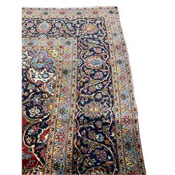 Persian Kashan carpet, red ground field with blue central medallion and spandrels, all-over floral design with stylised plant motifs and interlacing foliate, guarded border with scrolling designed decorated with floral motifs