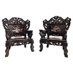 Pair early 20th century Chinese hardwood armchairs, the backs pierced and heavily carved with dragons and trailing flower heads, the seat backs with mother of pearl inlays depicting warriors with horses and traditional landscapes, the arms carved as a dragon with agape mouth and mother of pearl inlaid scales, scaled fish feet terminating to masks