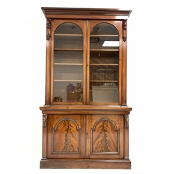 Victorian mahogany bookcase, projecting cornice over leaf and scroll carved corbels and two arched glazed doors enclosing four adjustable shelves, two panelled cupboards under enclosing a fixed shelf, on plinth base 