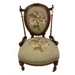 Victorian walnut nursing chair, the cresting rail carved with central foliate decoration and framing scalloped detail, the backrest flanked by turned and fluted column supports with roundel carved capitals, the back and sprung seat upholstered in floral needlework fabric, raised on turned and fluted supports terminating in brass and ceramic castors