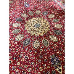 Persian design red ground carpet, the central floral medallion surrounded by stylised plant motifs and lanterns, the field decorated by interlacing foliate decoration, the guarded border decorated with repeating shaped floral panels 