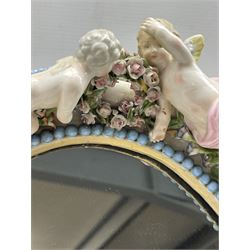 Pair of late 19th century Continental porcelain mirrors, of oval form, encrusted with flowers between borders of applied blue beads, surmounted by two putti and birds, another with musical instruments and two putti, both with scroll supports, mahogany back with easel support, 46cm x 32cm