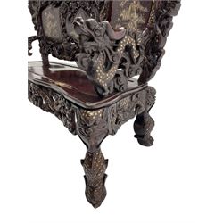 Early 20th century Chinese hardwood settee or hall-bench, the back pierced and heavily carved with dragons and trailing flower heads, the seat backs with mother of pearl inlays depicting warriors on horse-back and traditional landscapes, the arms carved as a dragon with agape mouth and mother of pearl inlaid scales, scaled fish feet terminating to masks