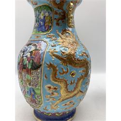 Pair of Chinese Canton Famille Rose twin handled vases, each of baluster form, decorated in low relief with four opposed shaped rectangular panels depicting dignitaries and attendants in a garden setting, the blue ground painted in iron red and gilded with dragons chasing the flaming pearl, within ruyi panel and greek key borders, unmarked, H30cm 