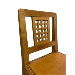 Mouseman - pair of oak dining or side chairs, pierced and carved lattice back over tan leather upholstered seat with stud band, on octagonal front supports joined by plain H-stretchers, by the workshop of Robert Thompson, Kilburn