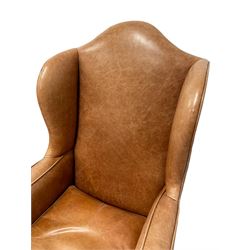 20th century hardwood framed wingback armchair, out swept and rolled arms with loose seat cushion, upholstered in tan leather with piping, on turned oak front supports with brass castors