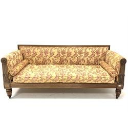 Early 19th century rosewood sofa, moulded crest rail and leaf carved arm terminals with floral roundels, back, seat, arms, and squab cushion upholstered in Nina Campbell pale gold fabric, raised on turned and lobe carved supports terminating in brass castors