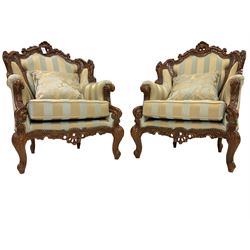Pair Italian Rococo style carved walnut finish wingback armchairs, pierced cartouche pediment with scrolling, back and seat upholstered in blue and gold fabric with studwork, scrolled hand rail raised by foliate scrolled uprights and cabriole supports