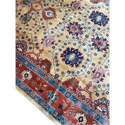 Persian Heriz pale camel ground carpet, the field with all-over palmette decoration and interlacing foliate branches, the guarded coral border with repeating stylised plant motifs and contrasting palmettes