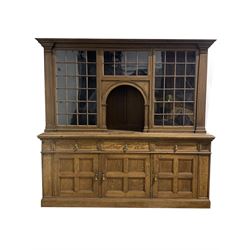 Liberty London - Early 20th century oak dresser, the top section with projecting cornice over three astragal glazed doors enclosing four shelves, decorated with fluted pilasters, over three drawers and three panelled cupboards each enclosing a shelf, raised on plinth base, bearing 
ivorine makers label to reverse, W206cm, H200cm, D56cm