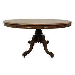Victorian rosewood loo table, the oval top over one carved and turned column, leading into four scrolled supports, terminating in brass castors 