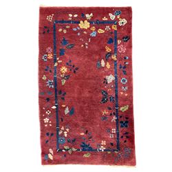 Early 20th century Chinese thick woollen crimson ground rug, the indigo border decorated with extending leafage and vines with coloured flower heads