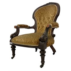 Victorian mahogany framed armchair, cresting rail carved with scrolling foliate cartouche over rolled arms, back and sprung seat upholstered in buttoned floral patterned mustard fabric, on turned and fluted supports with castors