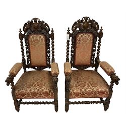 Pair of Victorian Jacobean Revival heavily carved oak armchairs, the pediment with central cartouche flanked by pierced and carved griffon motifs, the padded back surrounded by oak and scrolling acanthus leaves with flanking spiral turned uprights, back and sprung seat upholstered in red and gold urn patterned fabric, the arm terminals in the form of dog masks, on barley-twist supports united by spiral turned stretchers
