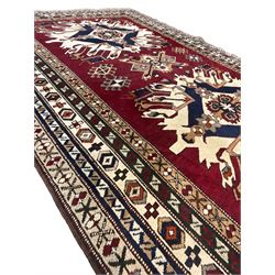 Turkish crimson ground rug, two central geometric medallions with ivory and indigo borders, the field decorated with stylised plant motifs, the multi-band border with repeating geometric designs 