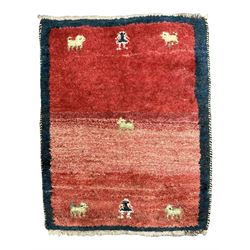 Small Persian Gabbeh crimson ground thick pile rug, decorated with stylised camel and figure motifs, encased with a plain indigo border, retailed by Fired Earth