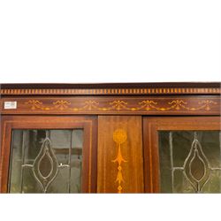 Edwardian Sheraton design inlaid mahogany display cabinet, the projecting cornice with inlaid boxwood checkered design over a frieze decorated with bellflower garland inlay, fitted with stained and lead glazed doors with an Art Nouveau tulip pattern, the interior with four shelves, raised on square tapering supports with spade feet