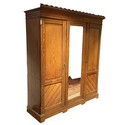 Late Victorian pitch pine triple wardrobe, projecting cornice over central mirror glazed doors and flanking panelled doors, the two left-hand doors enclosing four linen slides over two short and two long drawers, on plinth base