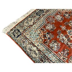 Persian Kerman red ground rug, the field with a central medallion surrounded by spaced floral garlands and bouquets, the secondary pale blue blue border with scrolling foliate vines and flower heads, the outer busy band with repeating plant motifs