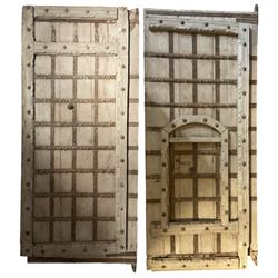 Pair of 18th to 19th century Continental hardwood gatehouse doors of rectangular form, the right-hand door fitted with a secondary door held within a carved applied hardwood support frame, each with wrought metal strapping with studwork, the railings applied with metal decoration in the form of stylised flowers, the metal handles with a spur circumference and loop handle