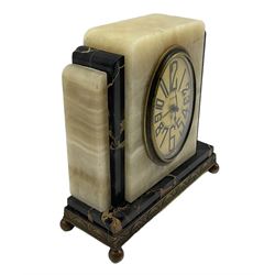A compact 20th century Fisco French Art Deco cream onyx and gold veined black marble alarm clock raised on a shallow brass plinth with ball feet, gilt oval dial with black Arabic numerals, spade hands and alarm indicator, , timepiece alarm movement with a pin pallet escapement, wound and set from the rear.