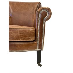 Pair traditional shaped armchairs, scrolled cresting rail and arms, upholstered in brown leather with studwork, on square supports with castors