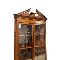 Edwardian inlaid mahogany and satinwood corner cabinet, the upper section with sloped broken dentil pediment, the frieze inlaid with central urn with extending linen swags, enclosed by two astragal glazed doors, the lower section with matching linen swag inlaid frieze over double cupboard, the panelled doors inlaid with scrolling leafy branches and flower heads, on bracket feet