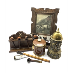 Early 20th century oak pipe rack with inset print, another with silver-plated stag mount, a 19th century brass tobacco jar and cover with tamper, decorated in relief with cherubs and Classical scenes