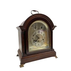 A German “Junghans” Westminster chiming mantle clock c1910, in an oak case with a break arch top and brass carrying handle, arch topped glazed door flanked by two reeded pillars with capitals, on a moulded plinth with  bracket feet, silvered sheet dial with chapter ring and subsidiary chime silent and pendulum regulation dials, with upright Arabic numerals, minute track and steel spade hands, three train eight-day movement chiming the quarters and hours on five gong rods. With pendulum.

