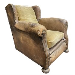 Early 20th century wingback armchair, upholstered in leather with stud work, turned front feet