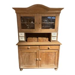 20th century pine dresser, the arched pediment with projecting cornice over two glazed doors enclosing pediment, with two small spice drawers to each upright, the lower section fitted with two panelled cupboard doors, raised on bun feet