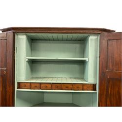 George III stained pine double corner cupboard, the projecting cavetto cornice over four panelled cupboard doors, the top section concealing a fitted interior with seven oak spice drawers and two shaped shelves, the lower section with single shelf, the interior painted a pale teal, raised on plinth base