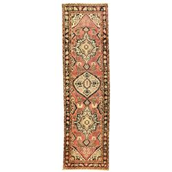 Persian rose ground runner rug, the field decorated with three floral medallions with dark indigo outlines, surrounded by stylised flower and urn motifs, guarded border with repeating foliate patterns