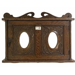 Early 20th century art nouveau period oak wall hanging cabinet, with stylised floral carving, two bevelled oval mirrors to door enclosing shelves W56cm 