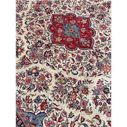 Large Persian Kashan carpet, the pale ground field decorated with shaped medallion and bunches of trailing flower heads and foliage, light blue and red ground spandrels with floral design, seven band border with overall floral design, the main band decorated with stylised plant motifs and trailing branch