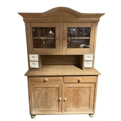 20th century pine dresser, the arched pediment with projecting cornice over two glazed doors enclosing pediment, with two small spice drawers to each upright, the lower section fitted with two panelled cupboard doors, raised on bun feet