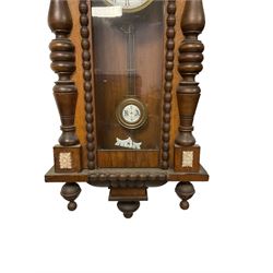 German - mid 19th century spring driven 8-day wall clock in an oak and mahogany case, with a turned and carved pediment, full length glazed case door flanked by ring turned columns and an ogee plinth with pendants, two part enamel dial with pierced steel hands, Roman numerals and minute track,  with a visible gridiron pendulum and striking movement, sounding the hours on a coiled gong.