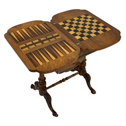 Victorian walnut games table, shaped fold-over and swivel top with chess, cribbage and backgammon boards, single drawer with divisions over sliding well, turned twin pillar base joined by turned stretcher, acanthus carved splayed supports with brass and ceramic castors