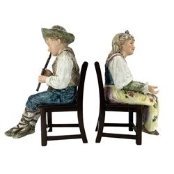 Pair of large Continental majolica musicians, modelled as a young boy and girl playing the tambourine and recorder, seated on associated chairs, H42cm overall