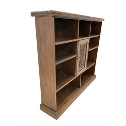 Open oak bookcase, the carved and moulded edge over seven shelves with one central carved cupboard, raised on a plinth base W165cm, H145cm, D38cm 