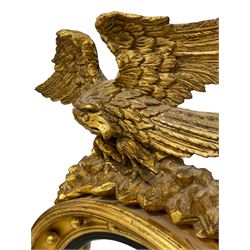 Regency gilt framed convex mirror, the eagle pediment with outstretched wings and turned head, surmounted on rocks, the circular plate with ebonised reeded slip within cavetto frame, applied with spherical mounts