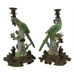 Pair of 20th century porcelain and brass mounted candlesticks, each modelled as a parrot atop a stump, with patinated brass sconce and naturalistic scroll base, H38cm. Provenance: From the Estate of the late Dowager Lady St Oswald