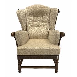 Ercol 'cloister' stained elm wingback armchair, with spindle back, fitted upholstered squab cushions, raised on turned and block supports united by stretchers W85cm