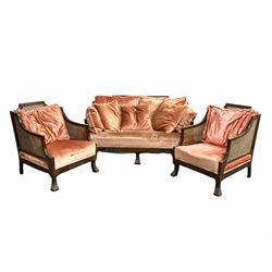 Early 20th century mahogany framed bergere lounge suite, the stepped cresting rail over single panel cane back,  swept arms with double cane panels, squab cushions and seat upholstered in crushed velour, raised on fluted scrolled and splayed supports () and pair of armchairs of a similar design