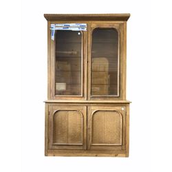 Large Edwardian oak and pine bookcase on cupboard, the cornice with geometric carved frieze over two arch glazed doors, each enclosing three adjustable shelves, two panelled cupboards under enclosing four further shelves, raised on a skirted base